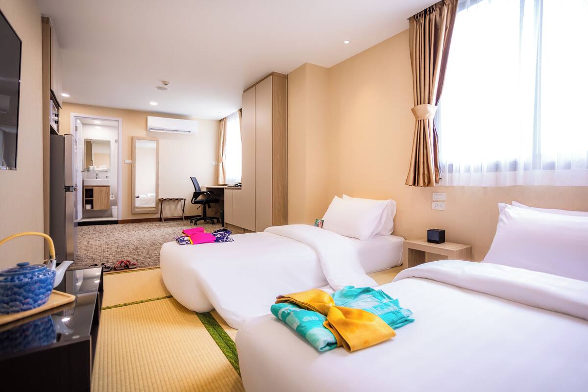 Une chambre d’hôtel avec deux lits, un bureau, une chaise, une télévision et une salle de bain visible à travers une porte ouverte.