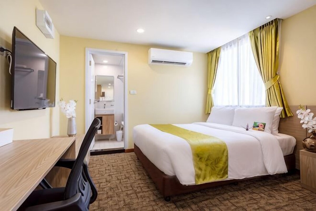 A hotel room with a bed, a desk, a chair, a television, an air conditioning unit, and a bathroom visible through an open door.