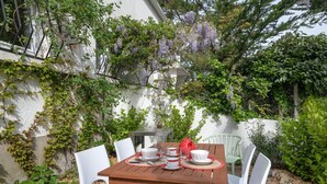 A wooden table set for tea with white chairs, surrounded by lush greenery and purple flowers. - 200m from the beach, cosy house for 4 (La Baule-Escoublac)