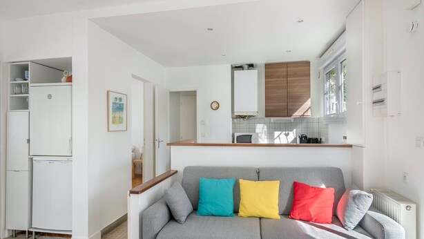 A compact living space with a kitchenette, a grey sofa with colorful cushions, and a white refrigerator. - 200m from the beach, cosy house for 4 (La Baule-Escoublac)