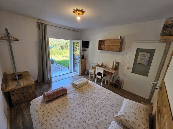 A bedroom with a bed, a desk, and a chair. There is a window with curtains, a door, and a map on the wall.