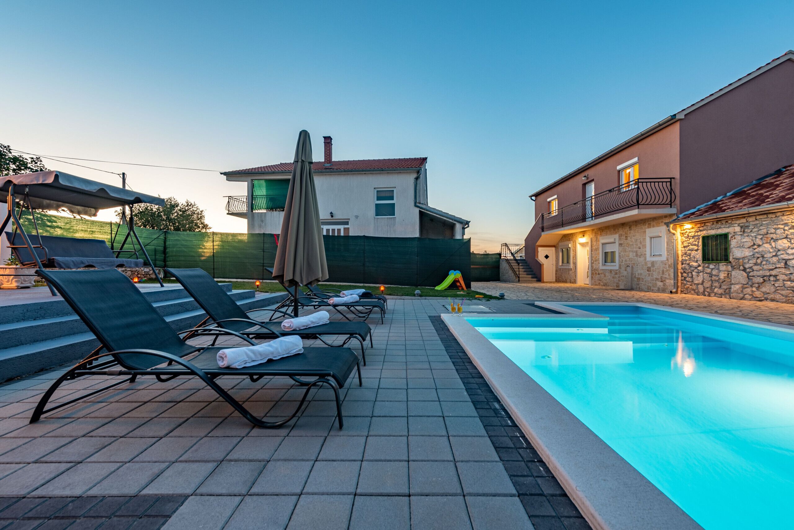 A swimming pool area with lounge chairs and a house in the background.