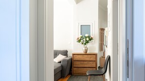 Ein Flur mit einem grauen Sofa, einem Holzschrank und einem Blumenstrauß.