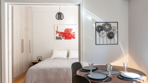 Ein modernes Schlafzimmer mit einem ordentlich bezogenen Bett, einem Nachttisch mit Lampe und einem Essbereich mit Tisch für zwei Personen.