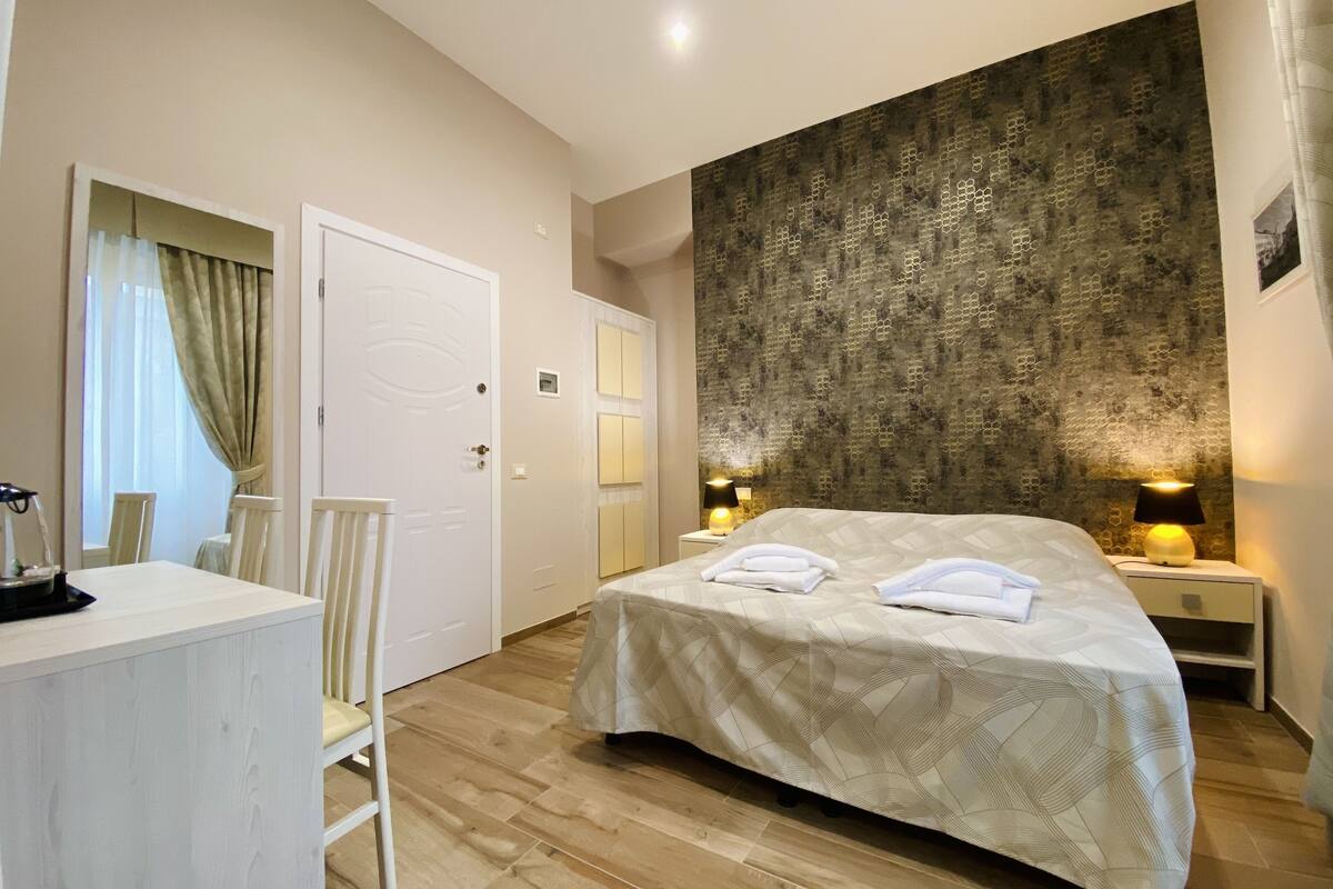 A hotel room with a bed, bedside tables, a desk, and a chair.