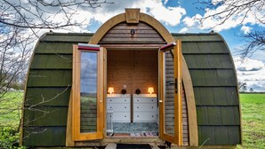 Une cabane en bois avec un toit en pente, dont les portes avant, ouvertes, révèlent un petit intérieur comprenant un banc et une table.