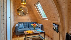 Une chambre à coucher confortable, aménagée en mezzanine, avec un plafond en pente, un canapé, une table basse ornée d’un vase de fleurs, un miroir et un téléviseur.