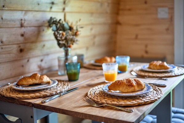 A wooden table with croissants on plates, a vase with dried flowers, and glasses of orange juice. - The Pods (Camerton)