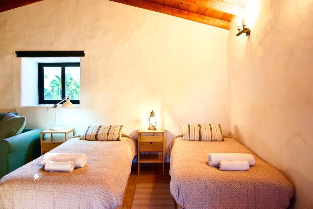 Een slaapkamer met twee bedden, een nachtkastje met een lamp, een raam en een groene stoel.