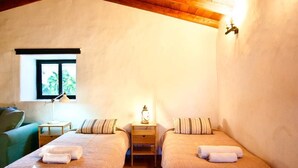 A bedroom with two beds, a nightstand with a lamp, a window, and a green chair.