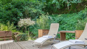 A wooden deck with two lounge chairs and a table, surrounded by lush greenery. - House By The Stream in Soca Valley (Kanal)