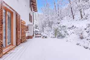 A snow-covered outdoor area with a wooden bench and a building with wooden shutters.