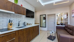 Une cuisine moderne avec des meubles en bois, des plans de travail blancs et un téléviseur encastré. On y trouve un canapé en cuir marron et une petite table avec une tasse et une soucoupe.