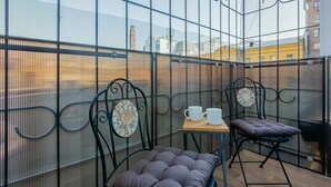 Un balcon avec deux chaises et une table, une paroi en verre et une vue sur les bâtiments en arrière-plan.