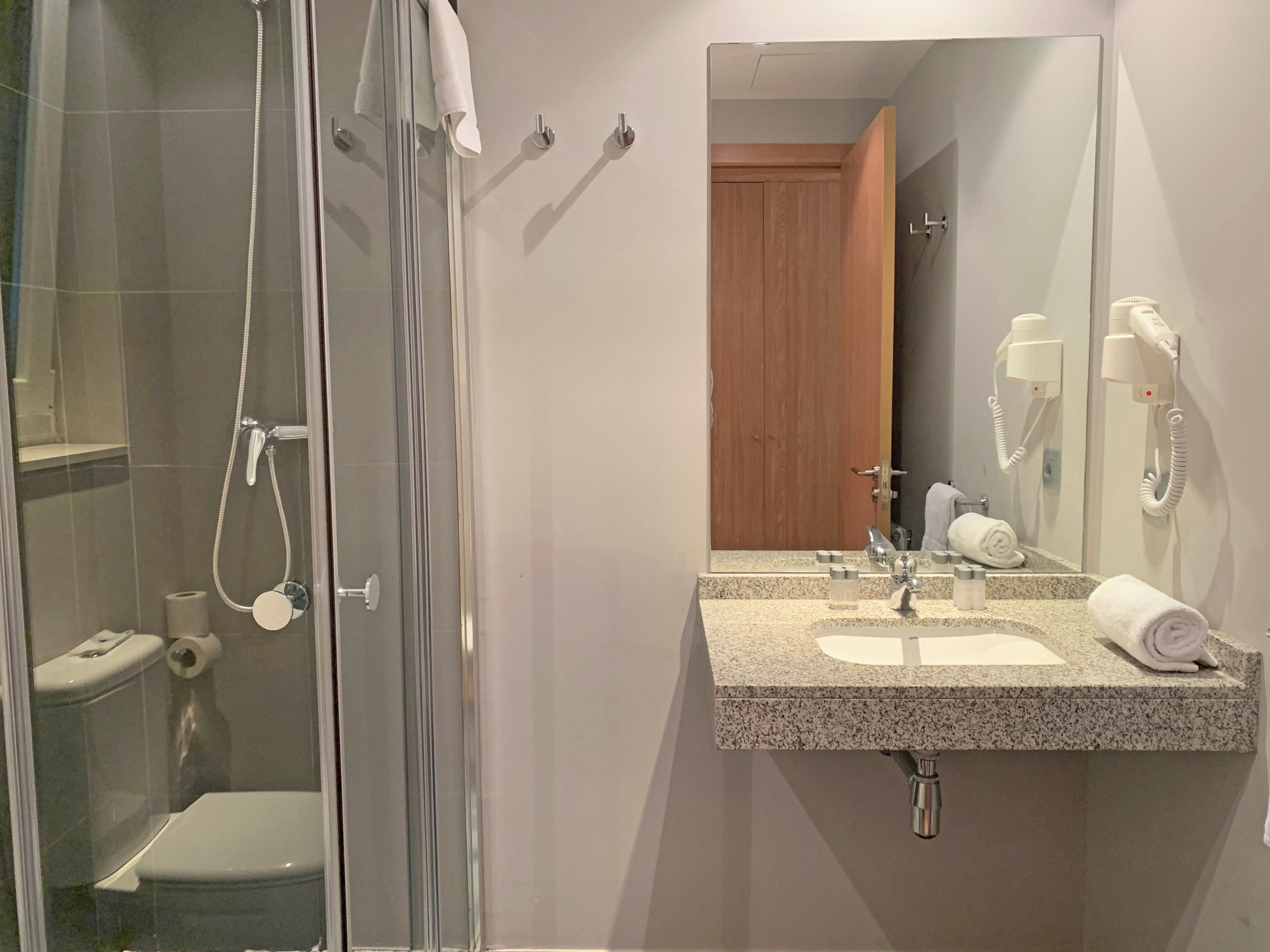 Une salle de bain dotée d’une douche à parois de verre, d’un lavabo avec un miroir et d’un sèche-cheveux fixé au mur.