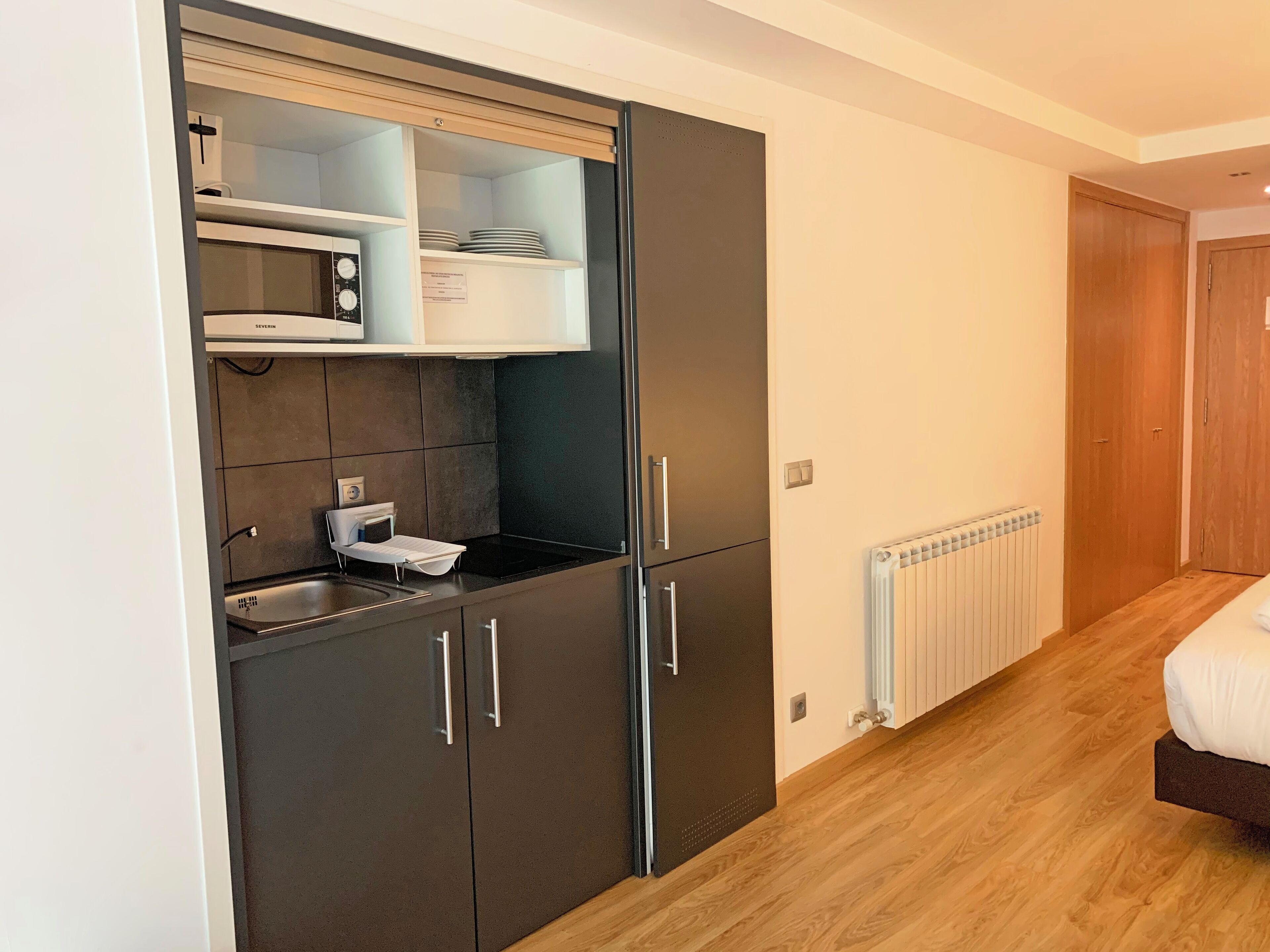 Una kitchenette compacta con microondas, pileta y placares, piso de madera y radiador.