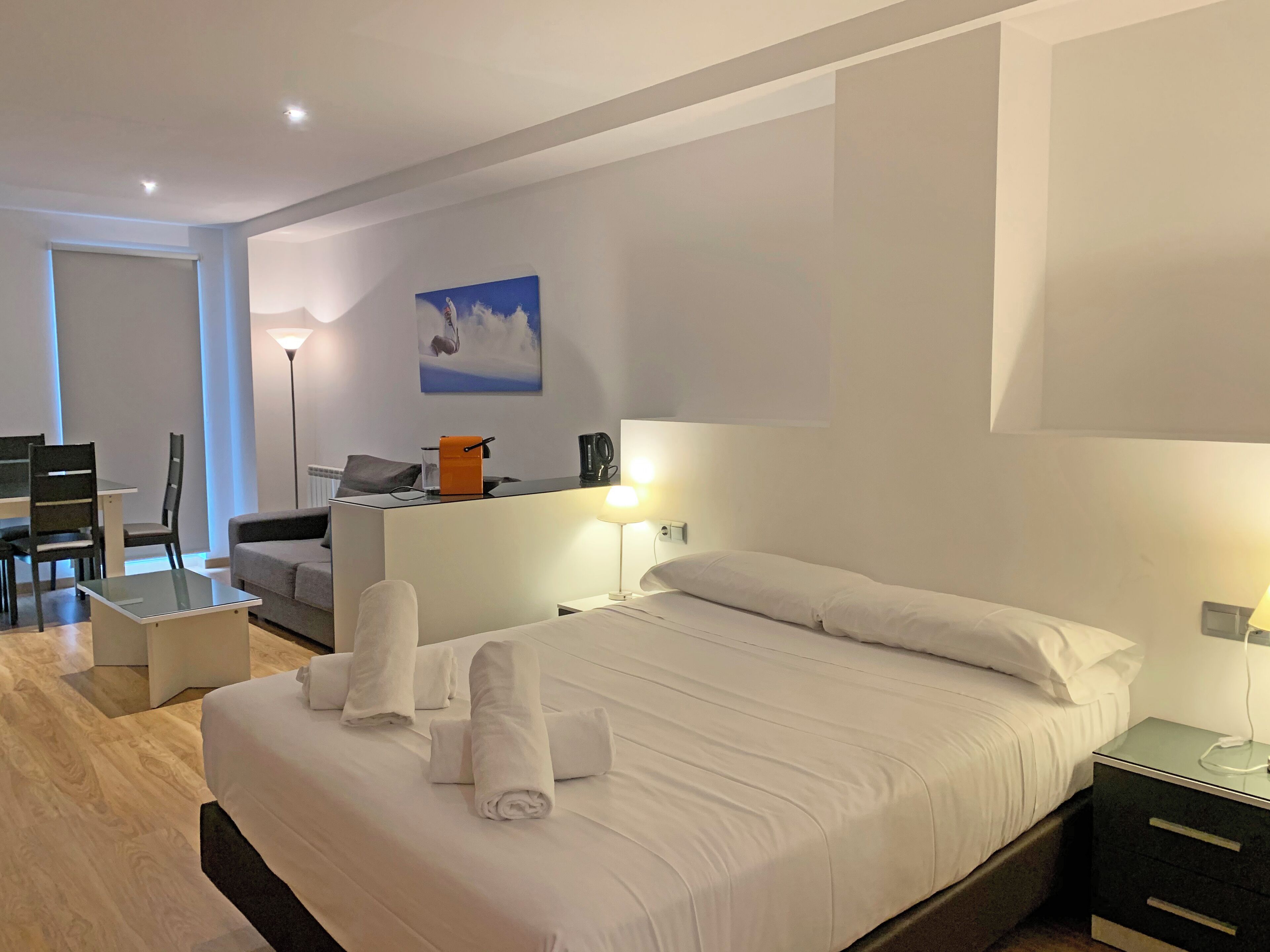 A hotel room with a bed, bedside tables, a desk, a chair, a lamp, and a painting on the wall.