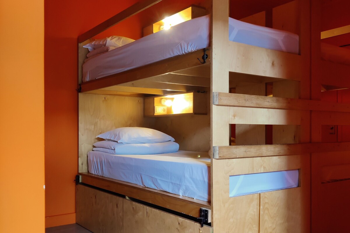 Een stapelbed met een houten frame, een klein raam en een lamp boven het bovenste bed.