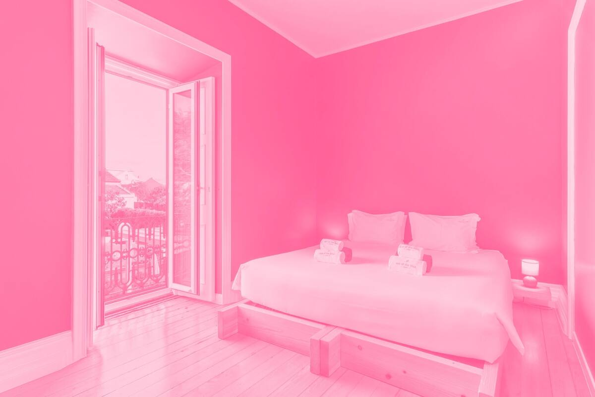 A pink-themed bedroom with a bed, bedside table, and a view through a glass door.
