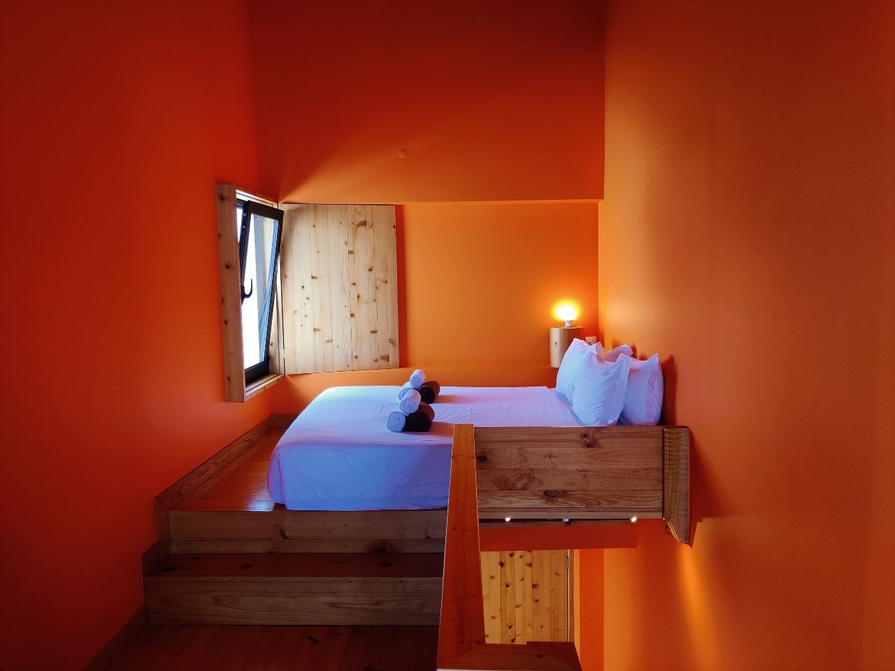 A room with a bed, a wooden bench, and a nightstand with a lamp.