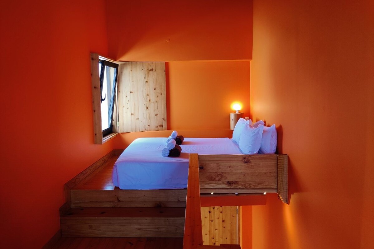 Een kamer met een bed, een houten bankje en een nachtkastje met een lamp.