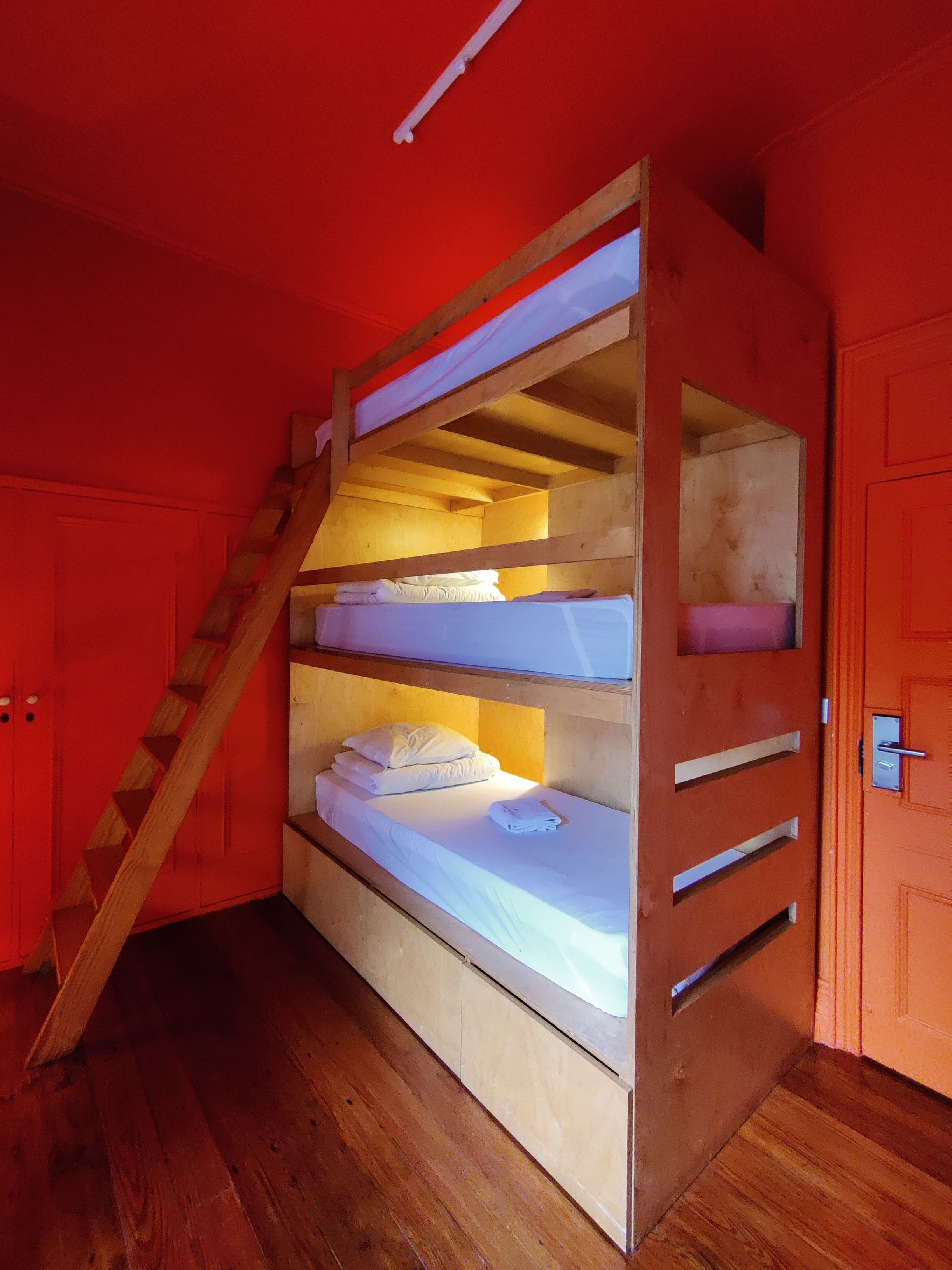 Un lit superposé avec une échelle en bois, un matelas blanc et un plancher en bois.