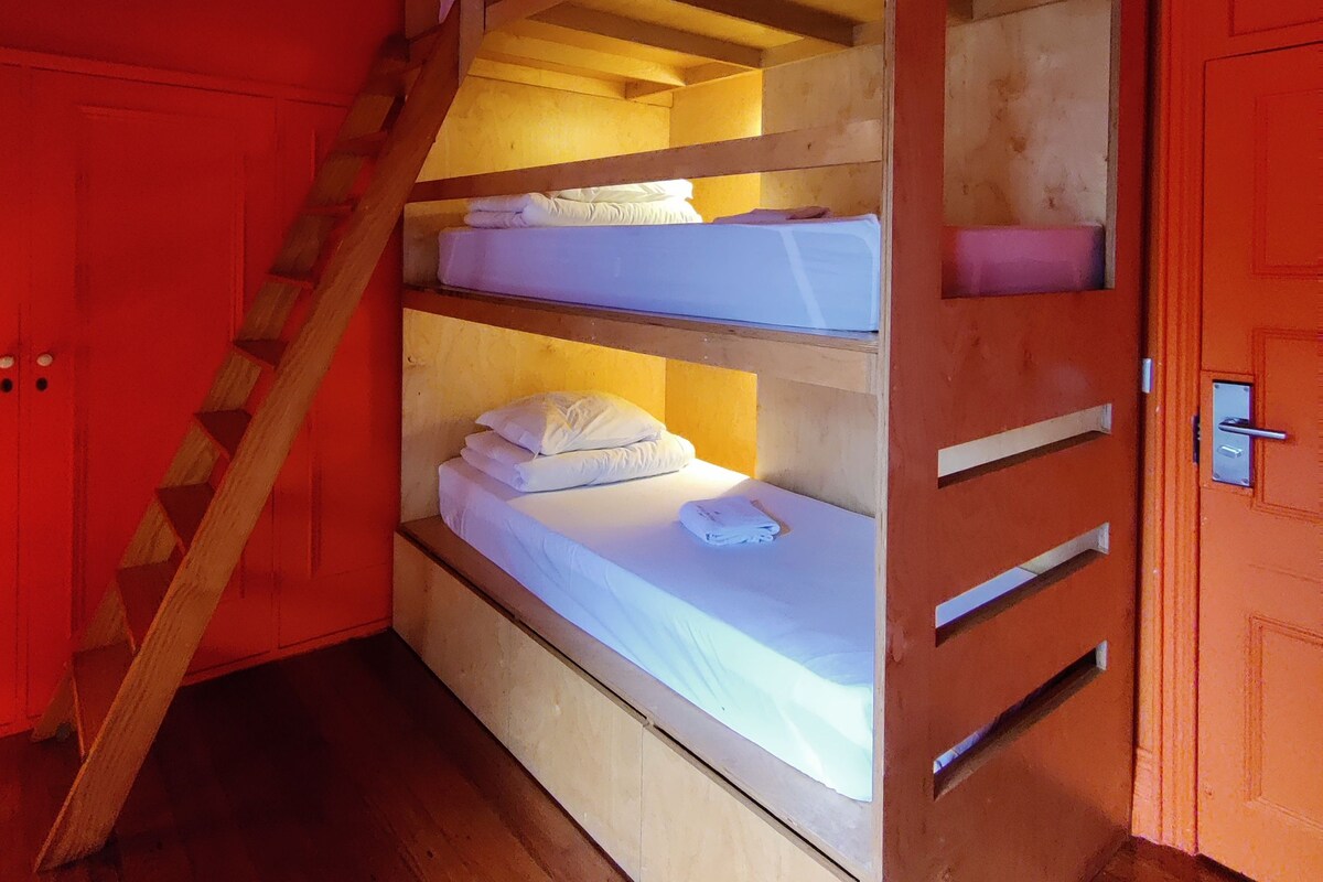 Een stapelbed met een houten trap, een wit matras en een houten vloer.