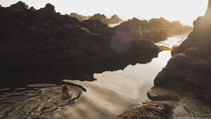 A rocky coastal landscape with calm water and a person in the water. - Out of the Blue - Hostel (Ponta Delgada)