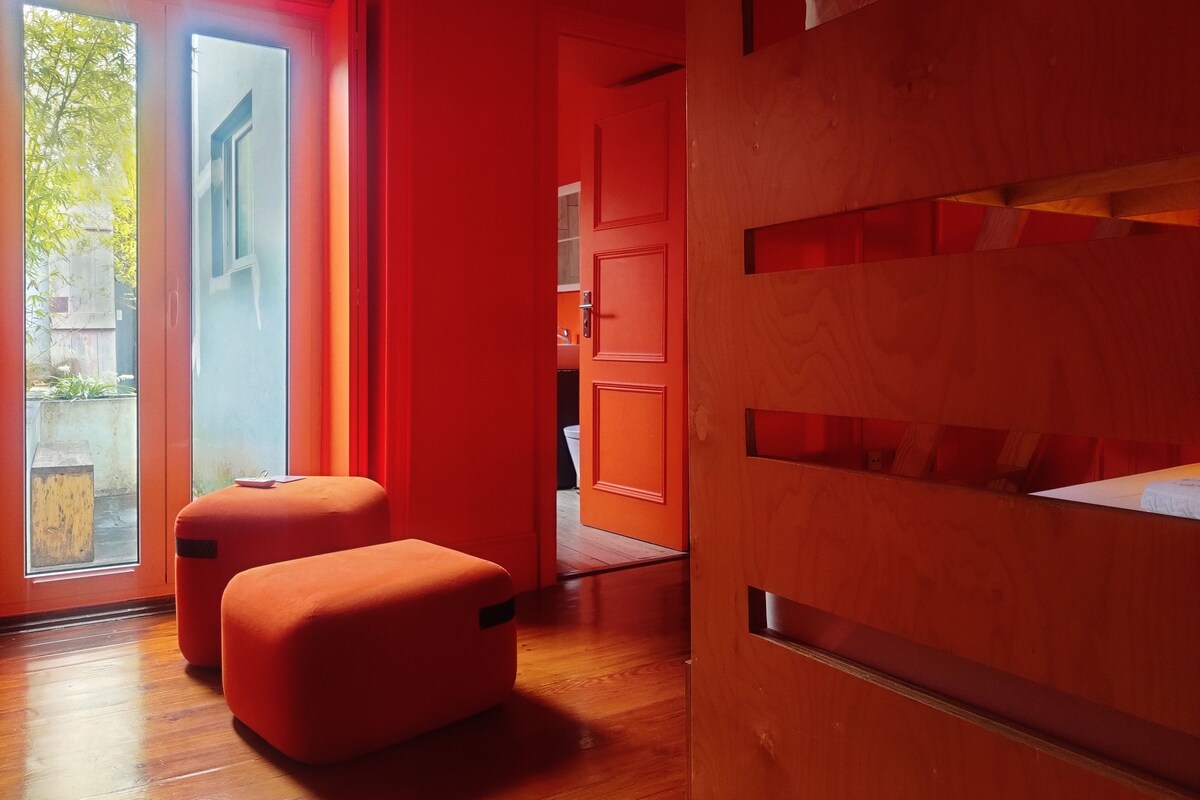 A modern interior with a red wall, wooden flooring, and a sliding glass door leading to an outdoor area.
