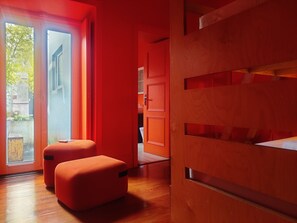 Un interior modern amb una paret vermella, terres de fusta i una porta corredissa de vidre que dona a zona exterior.