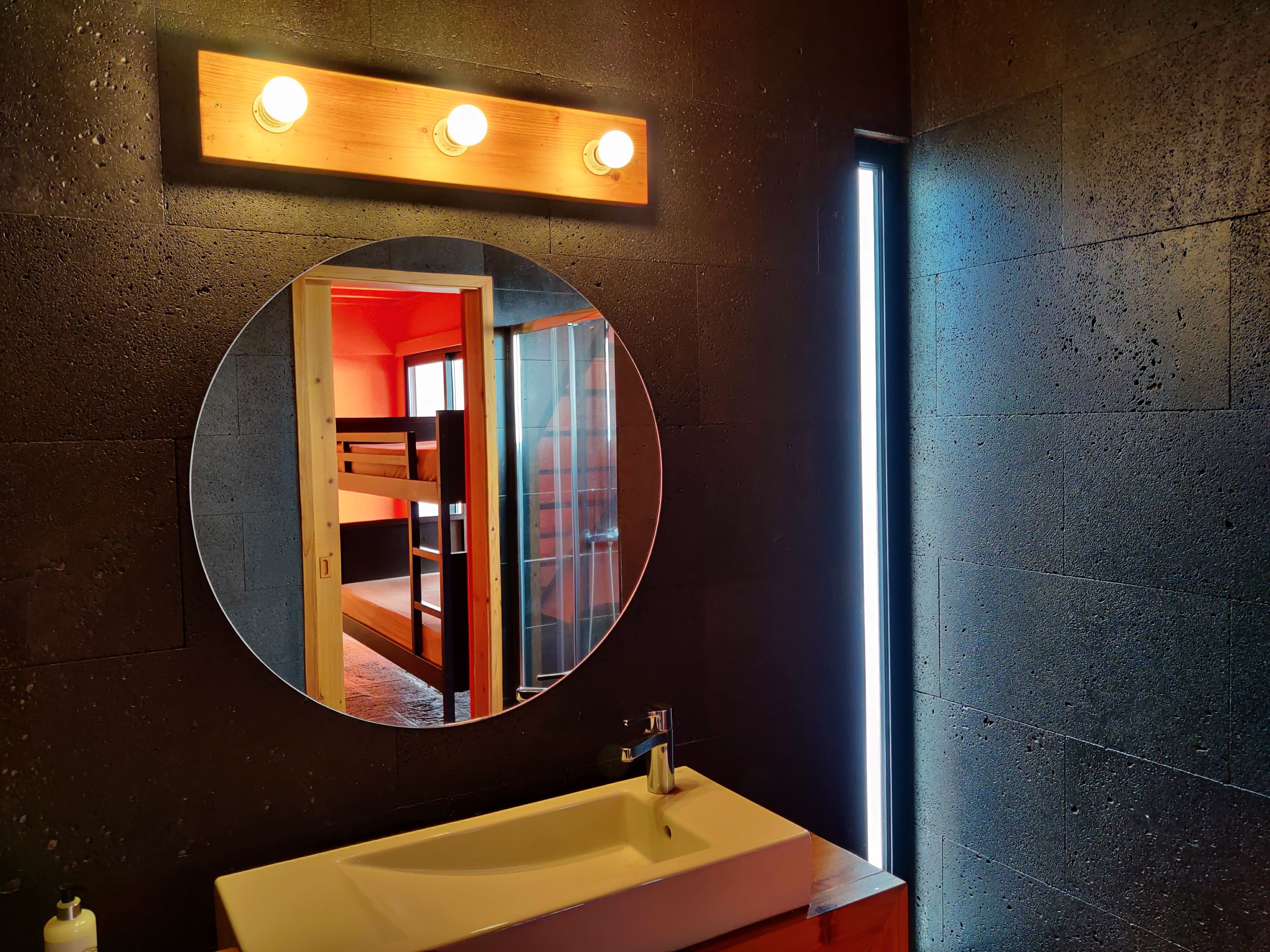 A bathroom with a round mirror, a sink, and a window.