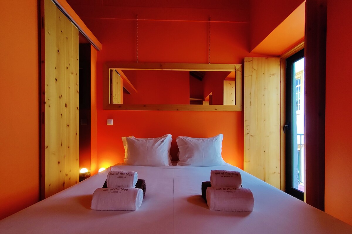 Een hotelkamer met een groot bed, twee kussens, een houten hoofdbord, een spiegel en twee handdoeken met tekst erop.