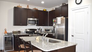 Una cocina moderna con gabinetes de madera oscura, electrodomésticos de acero inoxidable, encimera de granito y una isla integrada con taburetes de bar.