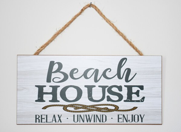 A sign with the words 'Beach House' and the phrases 'RELAX,' 'UNWIND,' and 'ENJOY.'