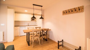 Een moderne keuken met witte kasten, een houten eettafel en twee stoelen. Daarboven hangt een lamp.