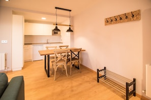 Une cuisine moderne avec des meubles blancs, une table à manger en bois et deux chaises. Un luminaire est suspendu au-dessus de la table.