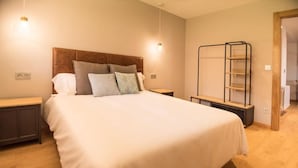 Een net opgemaakt bed met een houten hoofdbord, twee nachtkastjes en een wandplank.