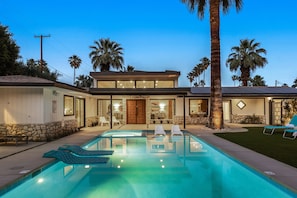 Uma casa moderna com piscina, palmeiras e fachada bem iluminada.