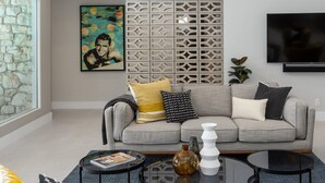 A modern living room with a grey sofa, a decorative wall panel, a flat-screen TV, and a glass coffee table.