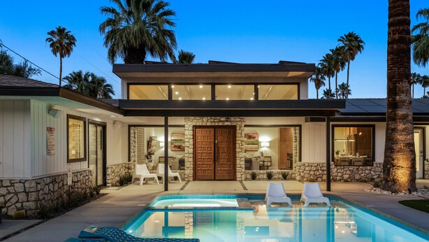 A modern house with a swimming pool, stone walls, and palm trees.