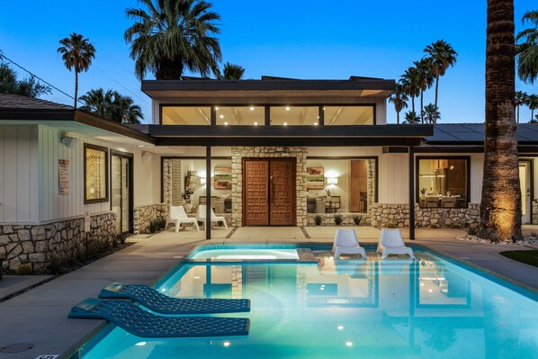 A modern house with a swimming pool, stone walls, and palm trees.