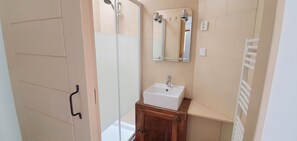 Un baño con cabina de ducha de vidrio, un lavabo blanco y un mueble de madera.