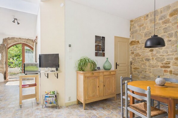 A cozy room with a wooden dining table, a television on a stand, a cabinet with decorative items, and a stone wall.