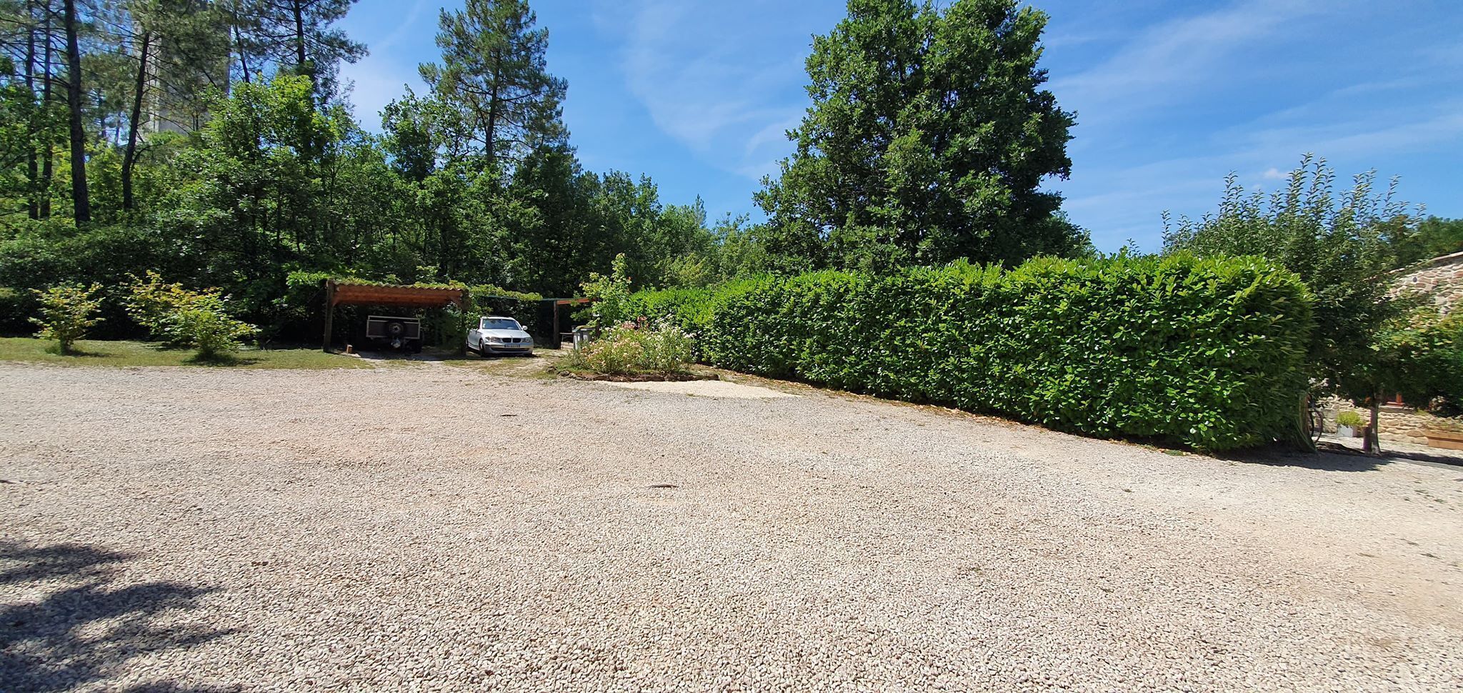 A gravel driveway leading to a covered car parking area with a vehicle parked inside.