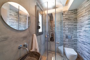 A modern bathroom with a glass-enclosed shower, a round mirror, and a wooden sink.