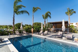 A pool area with lounge chairs and umbrellas, surrounded by palm trees.