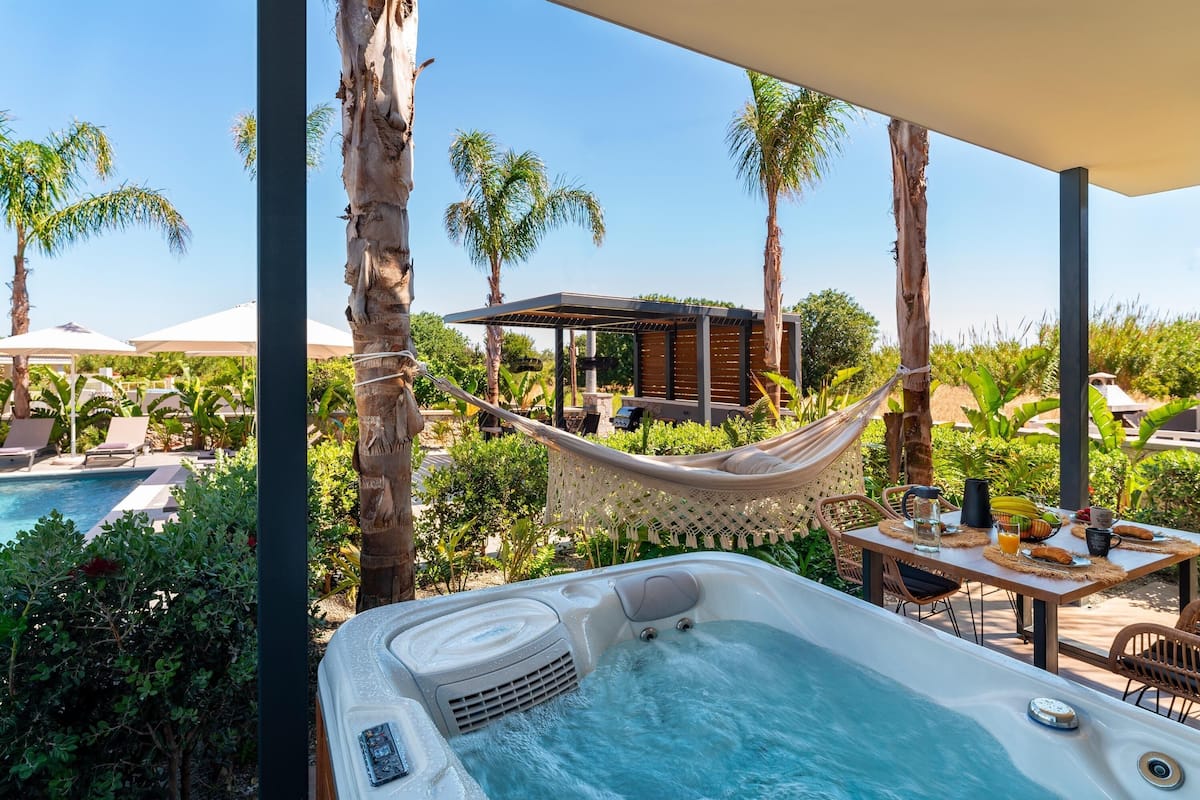 Ein Bereich mit Whirlpool, Tisch und Stühlen, umgeben von Palmen und einem Pool.