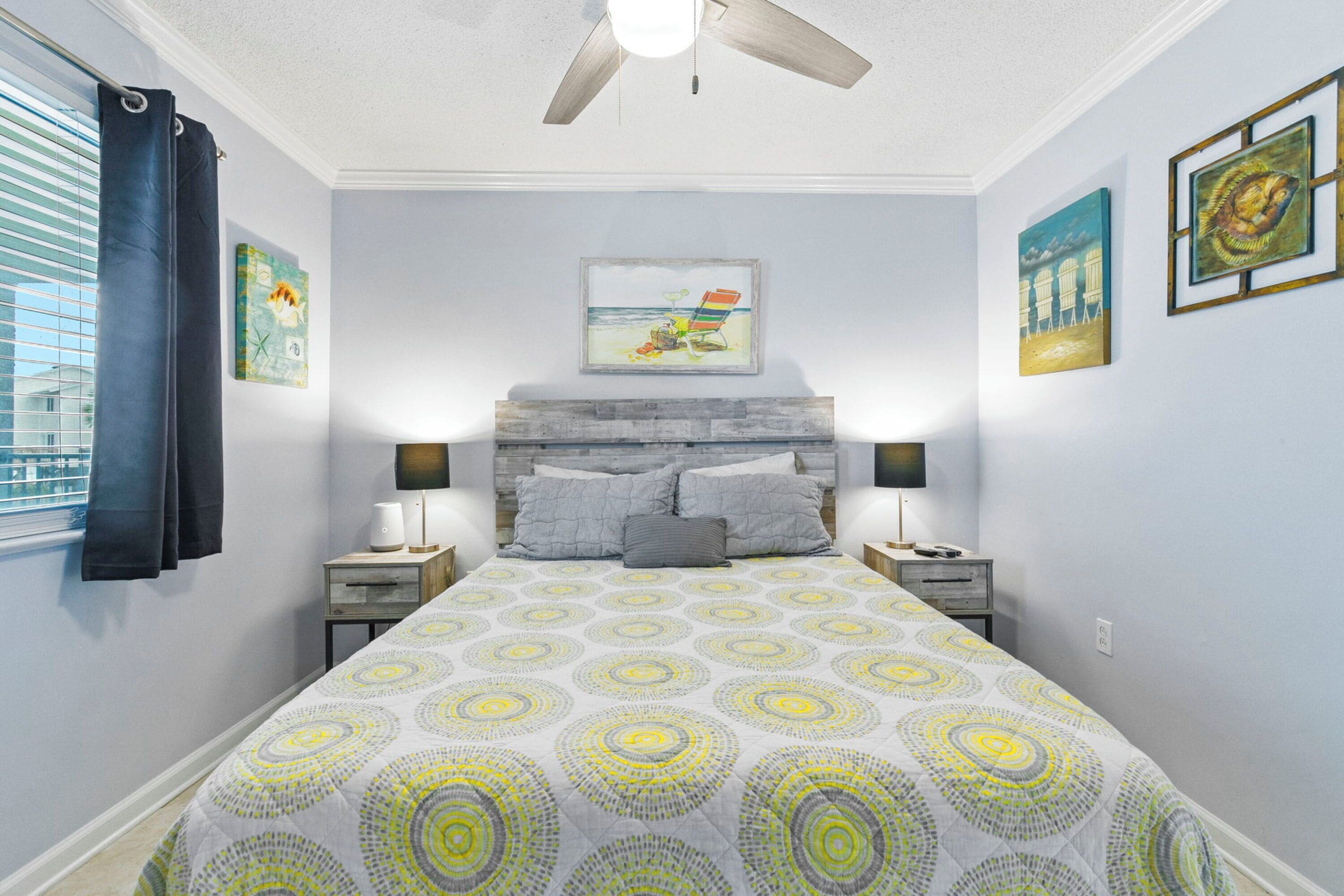 A bedroom with a bed, two bedside tables, a ceiling fan, and artwork on the walls.