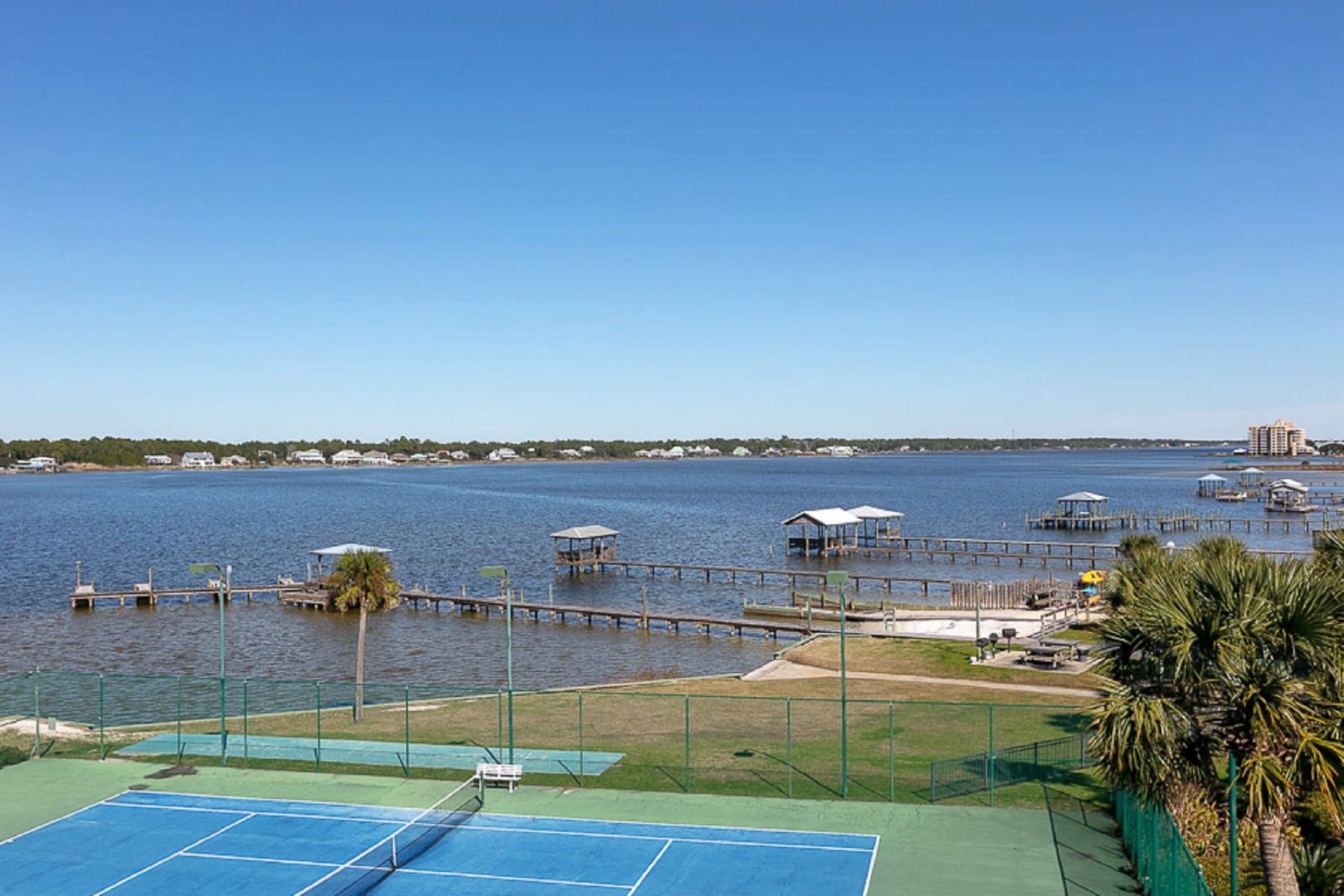 Una cancha de tenis con vistas a un lago y zona de embarcadero.