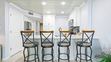 A kitchen with four bar stools, white cabinets, and a stainless steel refrigerator.